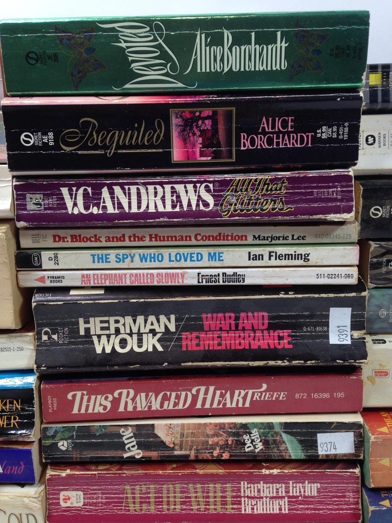 May include: A stack of vintage paperback books with titles including "Devoted," "Beguiled," and "War and Remembrance." The books have various colors and designs, with visible author names and publisher logos.