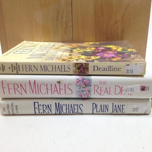 May include: Three paperback books by Fern Michaels are stacked. The top book is "Deadline" with a floral design. The middle book is "The Real Deal", and the bottom book is "Plain Jane". Each book has a white spine with the author's name.