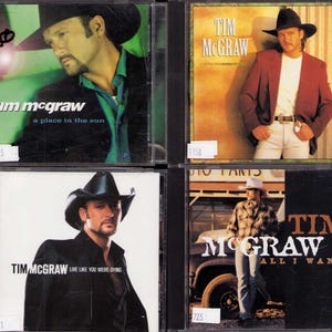 May include: Four Tim McGraw music CDs in plastic cases. Top left: A Place in the Sun. Top right: Tim McGraw self-titled album. Bottom left: Live Like You Were Dying. Bottom right: All I Want. Each cover features a portrait of the artist in a cowboy hat.