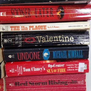 May include: A stack of paperback books with titles including "Firestarter," "Sooner or Later," and "The 11th Plague." The books are in various colors, with visible text and author names.