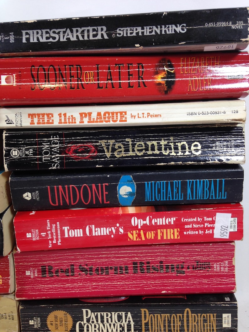 May include: A stack of paperback books with titles including "Firestarter," "Sooner or Later," and "The 11th Plague." The books are in various colors, with visible text and author names.