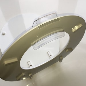 May include: A gold-colored toilet seat with a clear plastic lid. The seat is attached to a white base with four screws.