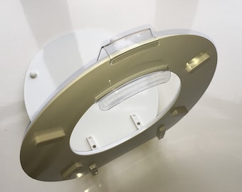 May include: A gold-colored toilet seat with a clear plastic lid. The seat is attached to a white base with four screws.