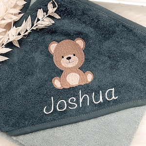Könnte beinhalten: Ein dunkelblaues Kapuzenhandtuch mit einem braunen gestickten Bären und dem Namen "Joshua" in weißer Stickerei.