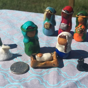 May include: A handmade nativity scene with a manger, baby Jesus, Mary, Joseph, three wise men, two sheep, a donkey, and a black cat. The figures are made of clay and painted in various colors.