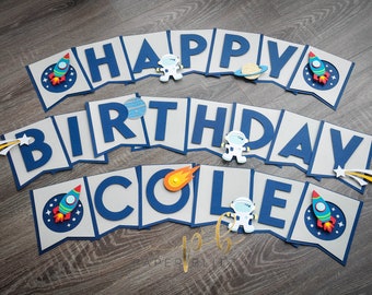 May include: A space-themed birthday banner with the words "HAPPY BIRTHDAY COLE" in blue letters on gray pennants. The banner is decorated with rockets, planets, astronauts, and shooting stars. Perfect for a space-themed birthday party.