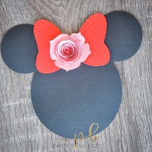 以下が含まれることがあります： 黒い紙で作ったミッキーマウスの耳の切り抜き。赤いリボンとピンクの紙の花が上に飾られています。画像の下には「PAPER BLITZ」という文字があります。