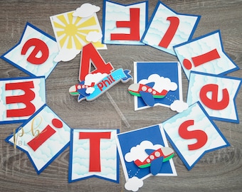 May include: A red and blue airplane themed banner with the letters "F I V E" and the number "4" with the name "Phil" on it. The banner is decorated with clouds and a sun.