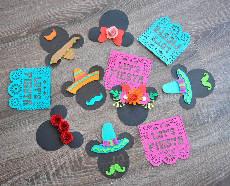 以下が含まれることがあります： 黒と白のミッキーマウスの頭の切り抜き9個セット。カラフルな紙の飾り付き。飾りには、ソンブレロ、花、そして「Let's Fiesta」と「Feliz Fiesta」と書かれた紙の旗が含まれています。