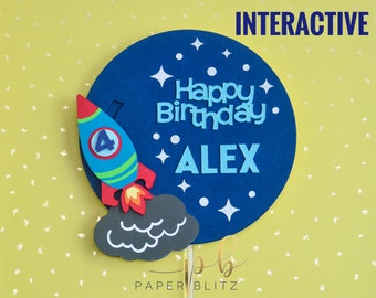 May include: Interactive cake topper featuring a blue rocket ship with a number 4 on the side, flying through a dark blue space with white stars and the text "Happy Birthday Alex".