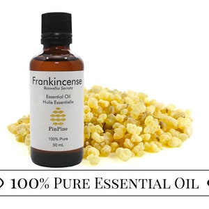 May include: A brown glass bottle with a label that reads "Frankincense Boswellia Serrata Essential Oil Huile Essentielle PinPine 100% Pure 50 mL". The bottle is sitting on a white surface next to a pile of yellow frankincense resin. The text "100% PURE ESSENTIAL OIL" is written on a white banner.