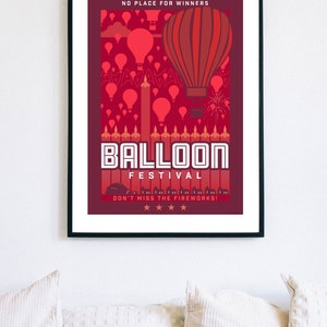 May include: A red and white poster with a black frame advertising a balloon festival. The poster features a large red hot air balloon with a red and white striped pattern. The text on the poster reads "No Place for Winners", "Balloon Festival", and "Don't Miss the Fireworks!"