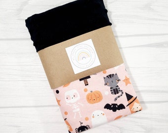 May include: A pink fabric with a Halloween print featuring a cat, a ghost, a skeleton, a pumpkin, a witch, a bat, and a spider. The fabric is wrapped in brown paper with a label that says "Little Tiny Designs".
