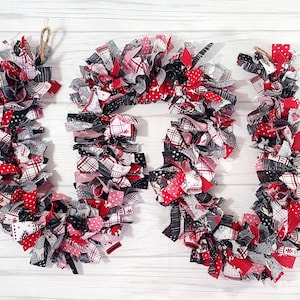 May include: A red, white, and black fabric Christmas garland with a plaid pattern. The garland is made of fabric scraps and is tied together with twine.