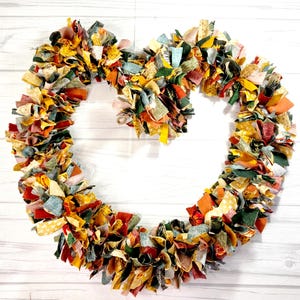 May include: A heart-shaped rag wreath constructed from numerous tied fabric strips in a variety of autumn-inspired colors including mustard yellow, burnt orange, forest green, and muted red, featuring various small-scale geometric and floral patterns.