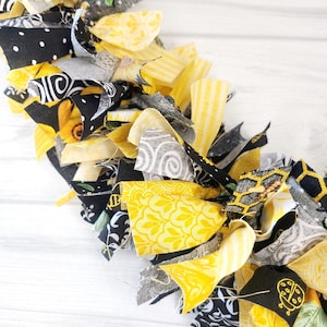 May include: A yellow and black fabric garland with a variety of patterns, including polka dots, stripes, and floral designs. The garland is made of fabric scraps that have been tied together.