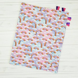 Op de afbeelding: Een zacht, roze en blauw babydekentje met een regenboog- en hartjespatroon. Het dekentje heeft paarse, roze en blauwe lintjes.
