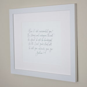 May include: A framed print with a white background and a gray inscription. The inscription reads "Have I not commanded you? Be strong and courageous. Do not be afraid; do not be discouraged, for the Lord your God will be with you wherever you go. Joshua 1:9"