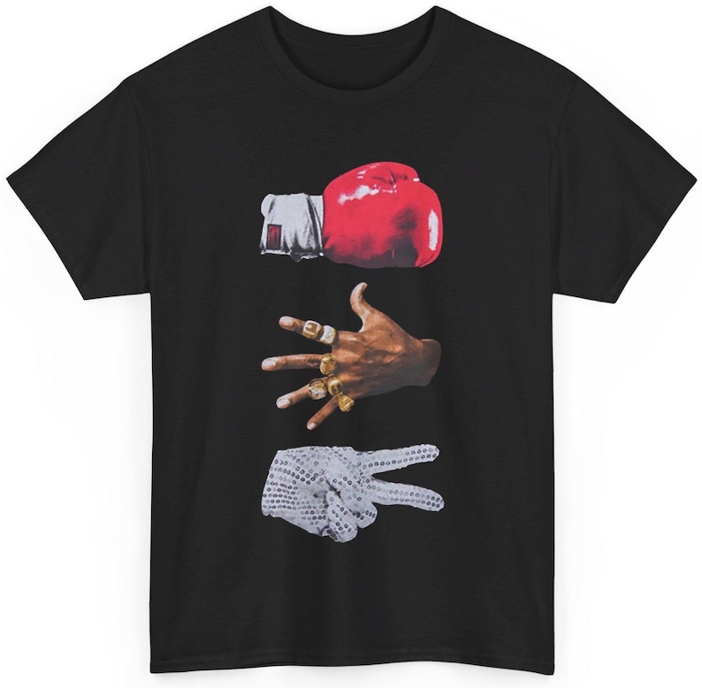 Peut inclure: T-shirt noir avec un motif graphique repr&eacute;sentant un gant de boxe rouge, une main orn&eacute;e de bagues dor&eacute;es et une main faisant le signe de la paix. Un design unique.