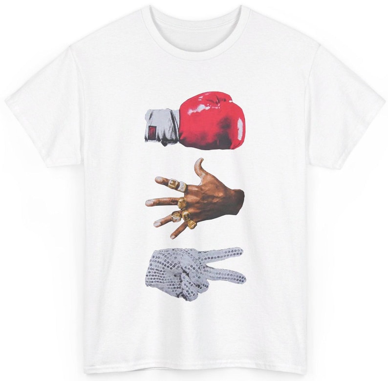 Peut inclure: T-shirt blanc avec un motif graphique de trois gestes de la main : un gant de boxe rouge, une main avec plusieurs bagues dor&eacute;es et un signe de paix avec un gant blanc. Col rond classique.
