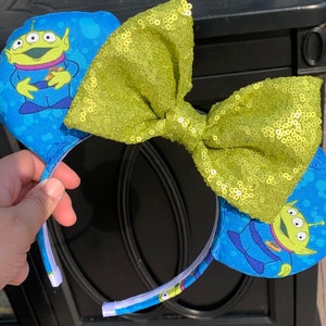 Pu&ograve; includere: Orecchie da topo blu con il personaggio alieno di Toy Story. Le orecchie hanno un fiocco di paillettes verde lime. La fascia &egrave; bianca con tessuto blu all'esterno. L'alieno &egrave; verde con tre occhi e indossa un'uniforme blu.