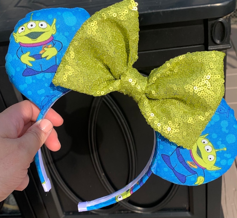 Pu&ograve; includere: Orecchie da topo blu con il personaggio alieno di Toy Story. Le orecchie hanno un fiocco di paillettes verde lime. La fascia &egrave; bianca con tessuto blu all'esterno. L'alieno &egrave; verde con tre occhi e indossa un'uniforme blu.