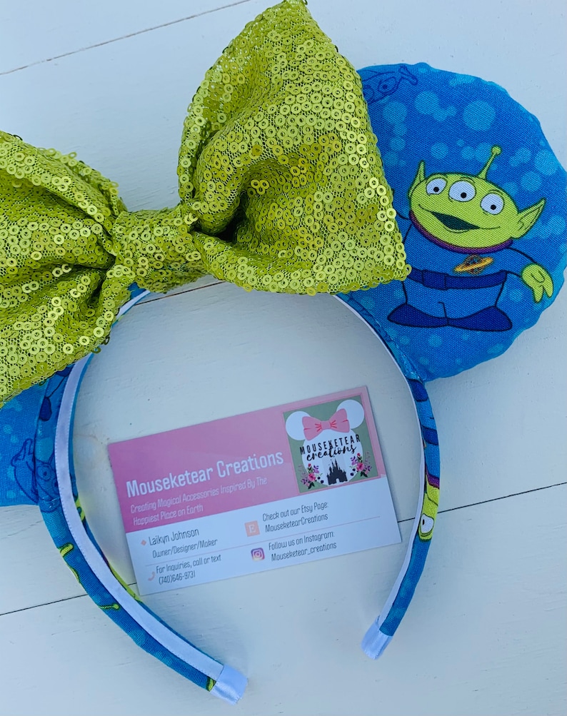 Pu&ograve; includere: Una fascia per capelli a tema Toy Story con orecchie blu stampate con un personaggio alieno e un grande fiocco di paillettes verde lime. La fascia ha un interno bianco e un biglietto da visita con il nome del marchio.