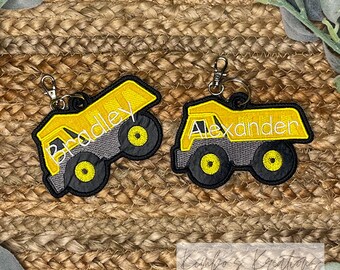 May include: Two yellow toy dump trucks with black wheels and gray details. The trucks are personalized with the names "Bradley" and "Alexander".