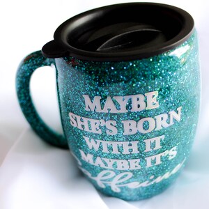 Peut inclure: Mug de voyage en paillettes turquoise avec un couvercle noir et le texte "Maybe she's born with it, maybe it's caffeine".