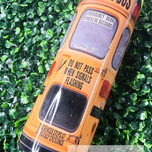 May include: A yellow school bus tumbler with the words "SCHOOL BUS" in black letters. The tumbler has a black stripe around the bottom and a black stripe around the top. The tumbler also has a black stripe around the middle with the words "EMERGENCY DOOR" and "PORTE DE SECOURS" in white letters. The tumbler also has a black stripe around the bottom with the words "THIS VEHICLE STOPS AT ALL RAILWAY CROSSINGS" in white letters. The tumbler also has a black stripe around the top with the words "DO NOT PASS WHEN SIGNALS FLASHING" in white letters.