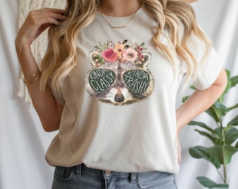 May include: A white t-shirt with a graphic of a raccoon wearing sunglasses and a flower crown. The sunglasses say "Kinda Classy Kinda Trashy".