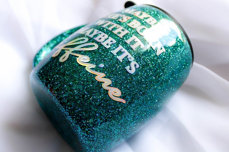 Peut inclure: Un gobelet en paillettes vert turquoise avec le texte "Maybe it's  because  we're  with it  maybe it's  coffee" en lettres blanches iris&eacute;es.