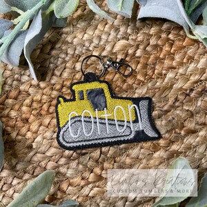 May include: Yellow and gray embroidered bulldozer keychain with the name "Cotton" on the side.