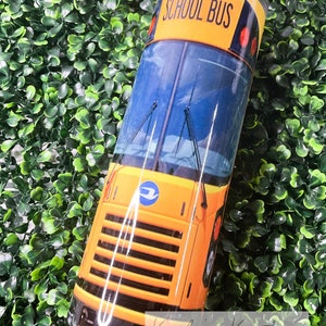 May include: Yellow school bus tumbler with the words "School Bus" printed on the side. The tumbler is on a green background.