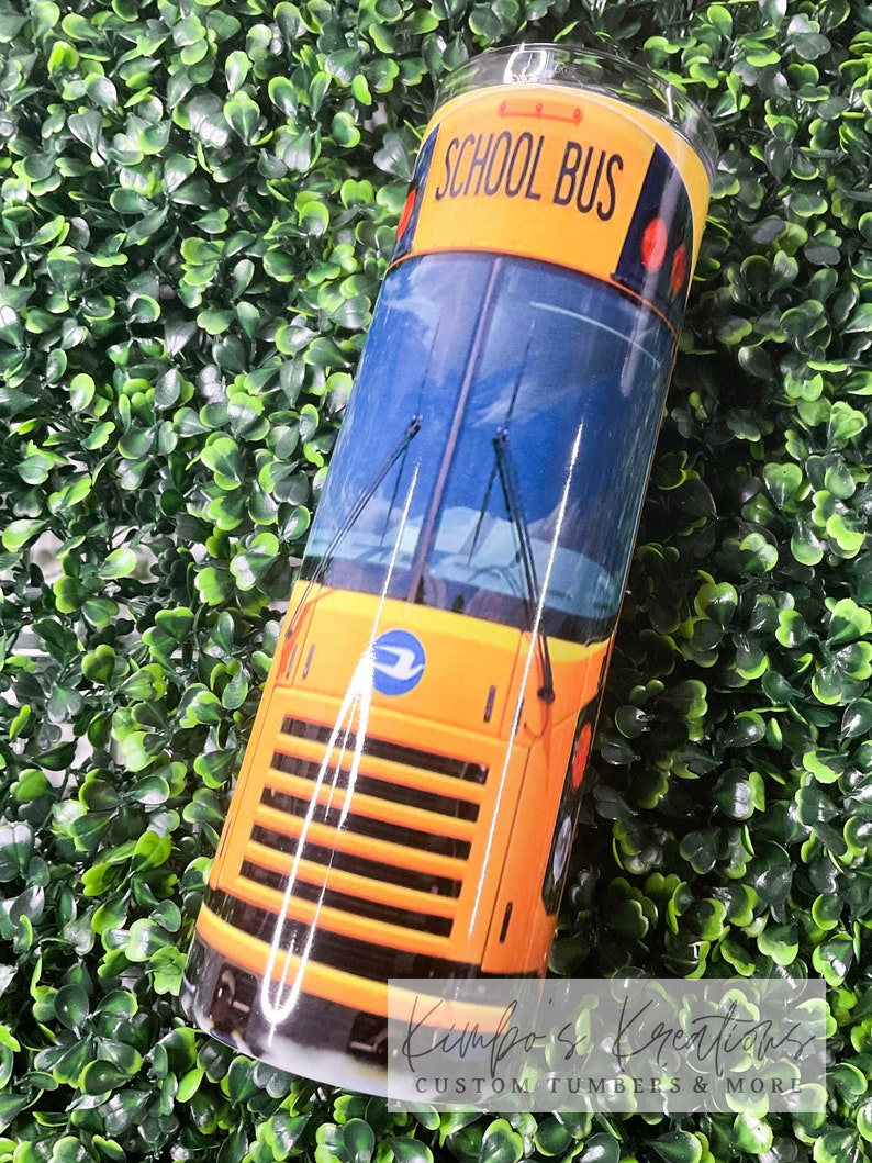 May include: Yellow school bus tumbler with the words "School Bus" printed on the side. The tumbler is on a green background.