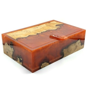 May include: A rectangular wooden box with a hinged lid. The box is made of wood and resin, with a natural wood grain pattern and a clear resin finish. The box is a rich orange color with brown and black accents.