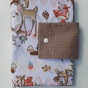 K&ouml;nnte beinhalten: Ein wei&szlig;er Stoffbuchumschlag mit einer braunen Tasche mit wei&szlig;en Punkten. Der Umschlag zeigt einen Waldtierdruck mit einem Reh, einem Fuchs, einem Kaninchen und Pilzen.