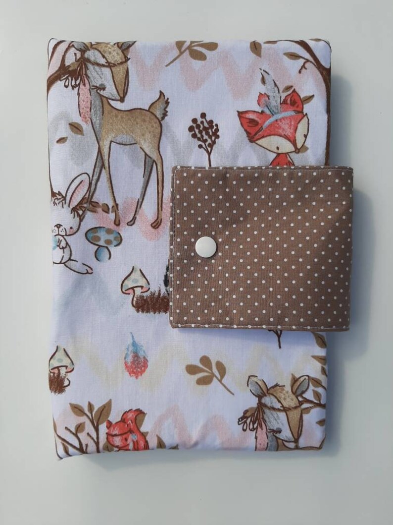 K&ouml;nnte beinhalten: Ein wei&szlig;er Stoffbuchumschlag mit einer braunen Tasche mit wei&szlig;en Punkten. Der Umschlag zeigt einen Waldtierdruck mit einem Reh, einem Fuchs, einem Kaninchen und Pilzen.