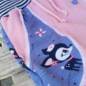K&ouml;nnte beinhalten: Rosa und blaue Kinderhose mit wei&szlig;er Spitzenborte und einem Hirschdruck. Die Hose hat einen gestreiften Bund mit einem Kordelzug.