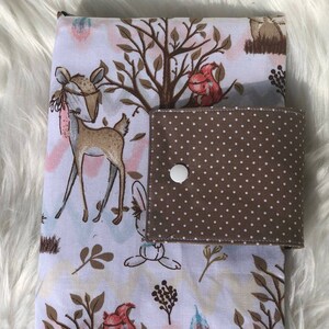 K&ouml;nnte beinhalten: Eine wei&szlig;e Wickelunterlage mit einer braunen und wei&szlig;en gepunkteten Tasche. Die Unterlage zeigt einen Wald-Druck mit Hirschen, Eichh&ouml;rnchen und Hasen.