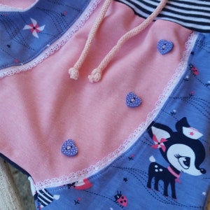 K&ouml;nnte beinhalten: Rosa und blaue Stoffhose mit wei&szlig;er Spitzenborte, einem schwarz-wei&szlig; gestreiften Bund und einem Kordelzug. Die Hose hat ein verspieltes Design mit Rehen, Marienk&auml;fern und Windm&uuml;hlen.