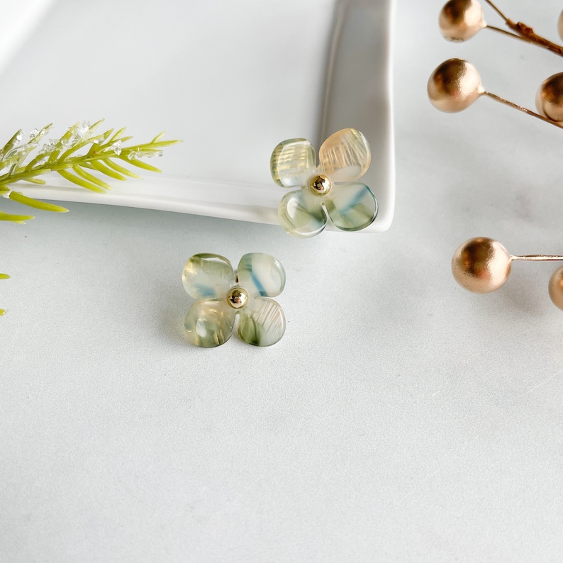 May include: A pair of green and gold flower-shaped earrings. The earrings are made of translucent plastic with a gold centre.