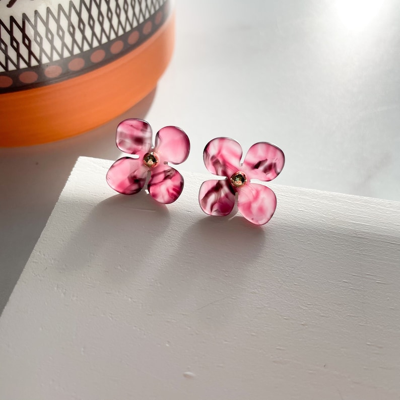 May include: A pair of pink flower-shaped earrings with a gold centre. The earrings are made of a marbled material.