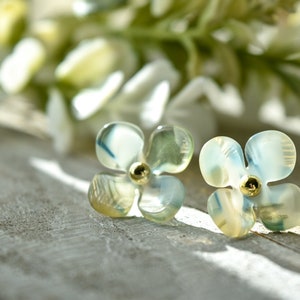 May include: A pair of delicate flower-shaped earrings with a light blue and green iridescent finish. The earrings have a gold centre with a small bead.