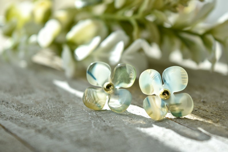 May include: A pair of delicate flower-shaped earrings with a light blue and green iridescent finish. The earrings have a gold centre with a small bead.