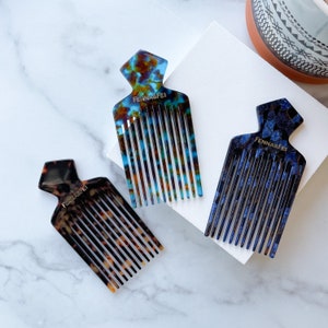 K&ouml;nnte beinhalten: Drei Schildpattk&auml;mme mit einem einzigartigen Design. Die K&auml;mme sind aus geflecktem braunen, blauen und t&uuml;rkisfarbenen Kunststoff. Die K&auml;mme haben ein breites Zahn-Design und sind mit "Fenna & Fei" beschriftet.
