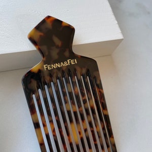 K&ouml;nnte beinhalten: Ein Kamm aus Schildpatt mit einer einzigartigen, spitzen Oberseite. Der Kamm tr&auml;gt eine goldene Inschrift mit der Aufschrift "Fenna & Fei".