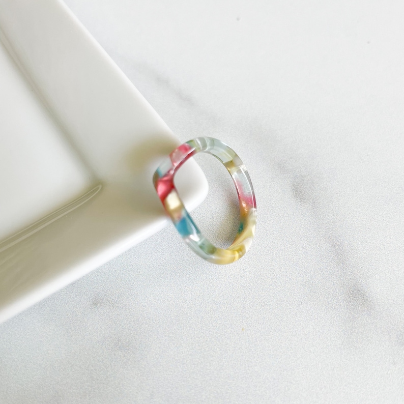 May include: A colorful, translucent ring with a swirl pattern in shades of pink, blue, yellow, and green.