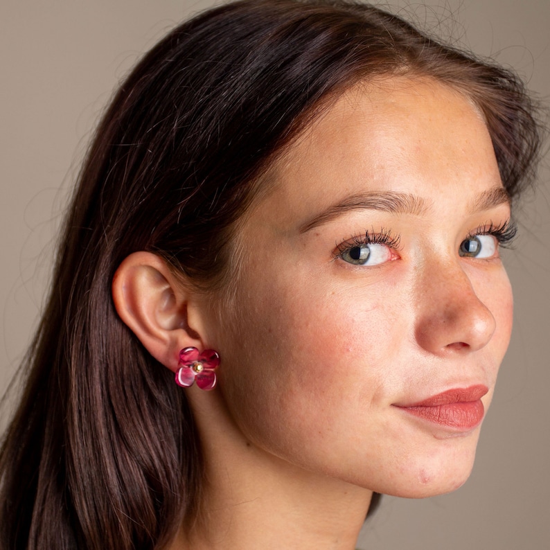May include: A woman wearing a pair of pink flower-shaped earrings. The earrings have a gold centre.