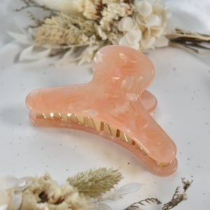 May include: A large peach-colored hair claw with a gold metal bar. The claw has a swirl pattern and is made of a translucent material.
